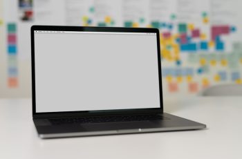 laptop on a table with a blank screen, background with colorful sticky notes